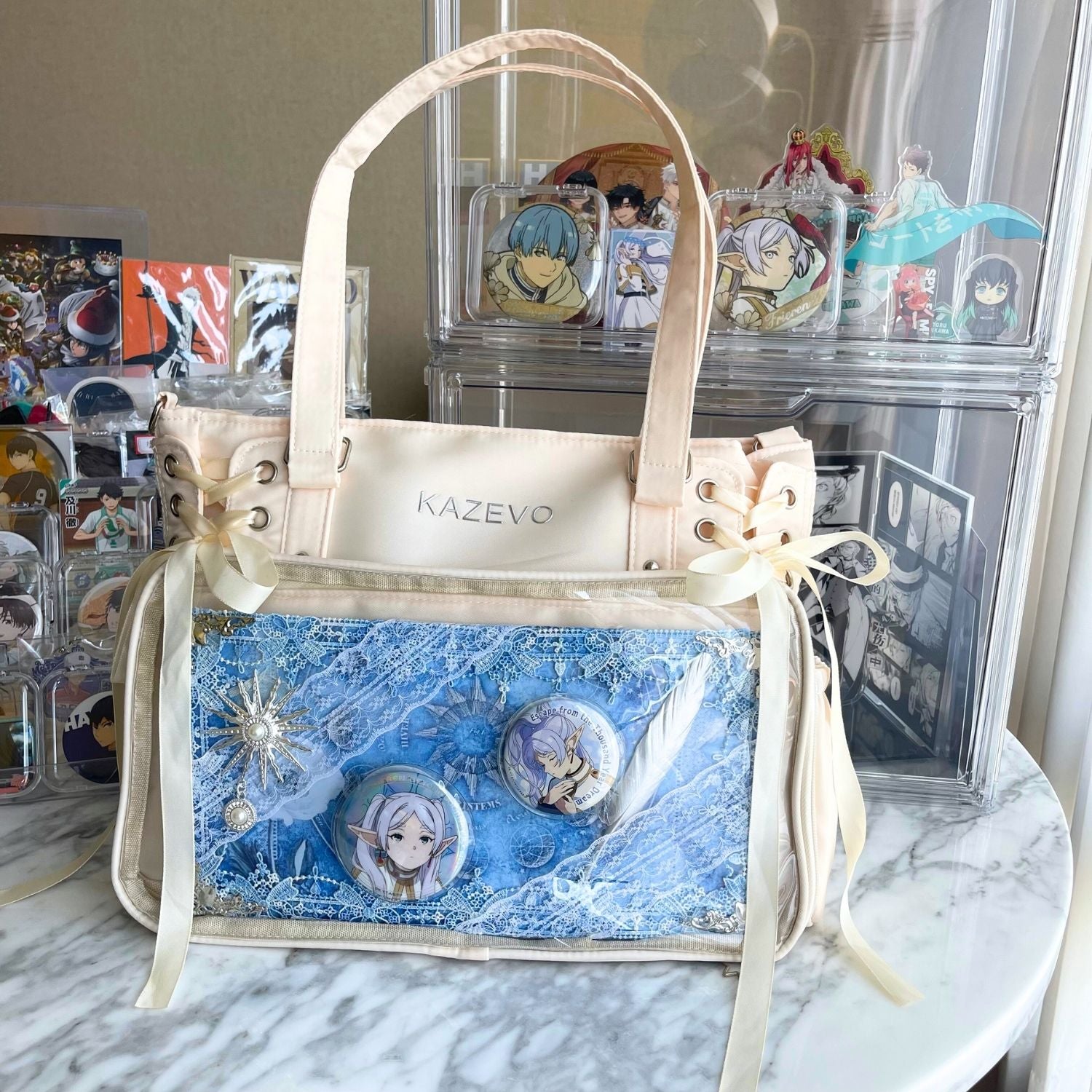 white cream color ita bag on table with decorated ita board filled with anime Frieren badges and pins inside clear window