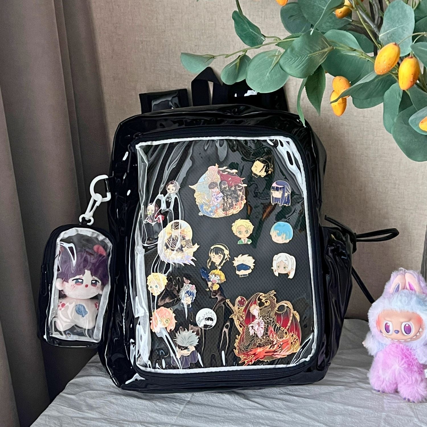 super large ita backpack on table with enamel pins inside clear window and plushie in attached mini plush bag